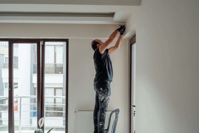 Worker on a ladder repairing drywall where the wall meets the ceiling