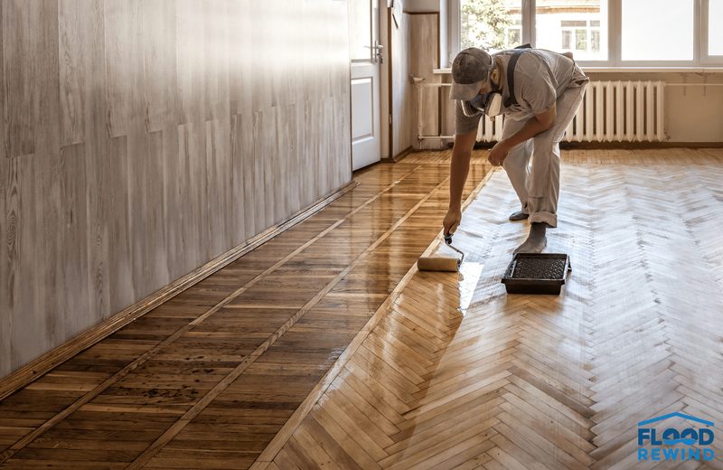 Worker on knees working on a wood floor in a room with new wall paneling