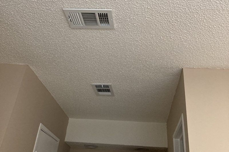 Hallway ceiling after a drywall patch, retextured and painted to match, with air vents and freshly painted beige walls