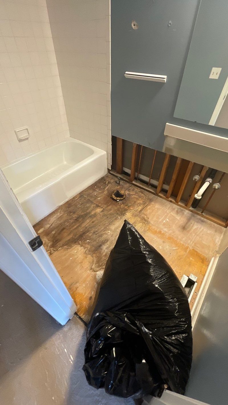 Bathroom with the old flooring torn out and the lower walls opened next to the tub
