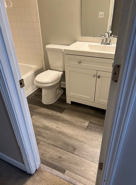 Finished bathroom with new wood-look flooring and white vanity after residential reconstruction